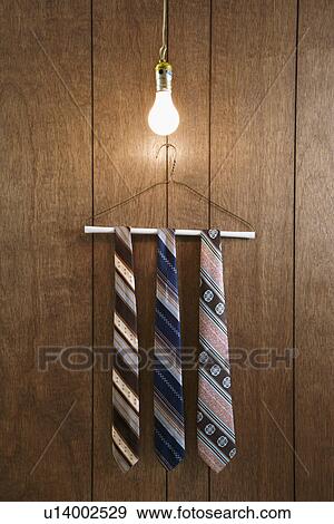 Stock Photo - Three retro ties hanging on a wire hanger against wood paneling with a glowing lightbulb hanging down from above.. Fotosearch