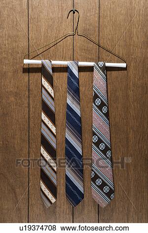Stock Photo - Three retro ties hanging on a wire hanger against wood paneling. Fotosearch