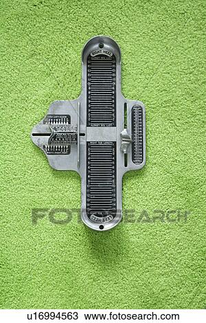 Stock Image - Vintage foot size measuring device against green carpet. Fotosearch