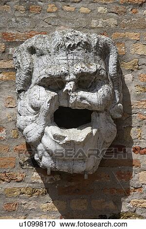 Stock Image - Weathered and broken concrete head hanging from brick wall. Fotosearch