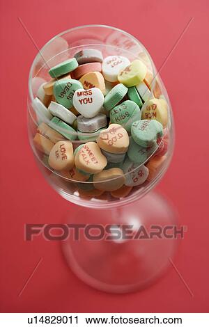 Stock Image - Wine glass full of colorful candy hearts with sayings on them on red background.. Fotosearch