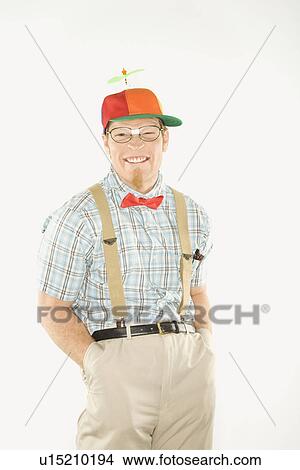 Picture - Young man dressed like nerd wearing propeller cap with hands in pockets looking at viewer with big smile. Fotosearch