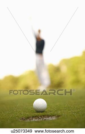 Close-up of a golf ball on the edge of a hole with a man standing in the background View Large Photo Image Stock Photo - Close-up of a golf ball on the edge of a hole with a man standing in the background. Fotosearch