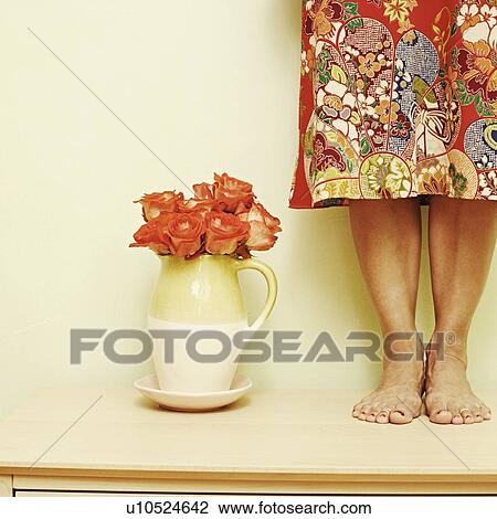 Stock Image - Low section view of a woman standing on the table. Fotosearch