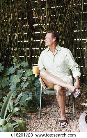 Stock Image - Mature man sitting on a chair and holding a mug. Fotosearch
