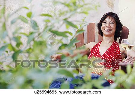 Mature woman sitting on a chair and holding a glass of white wine View Large Photo Image Stock Photography - Mature woman sitting on a chair and holding a glass of white wine. Fotosearch