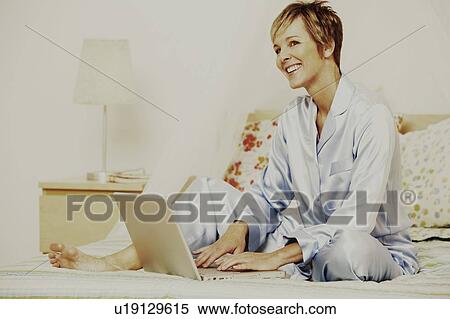 Mature woman using a laptop on the bed and smiling View Large Photo Image Stock Photography - Mature woman using a laptop on the bed and smiling. Fotosearch
