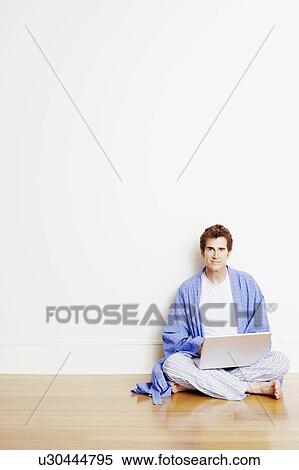 Stock Photography - Portrait of a mature man sitting cross-legged on the floor and using a laptop. Fotosearch