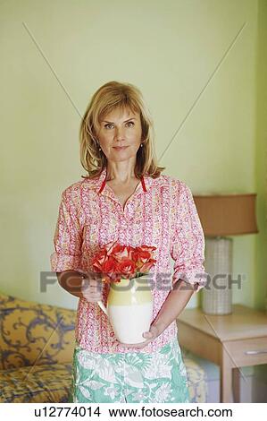 Picture - Portrait of a mature woman holding a pitcher with flowers. Fotosearch