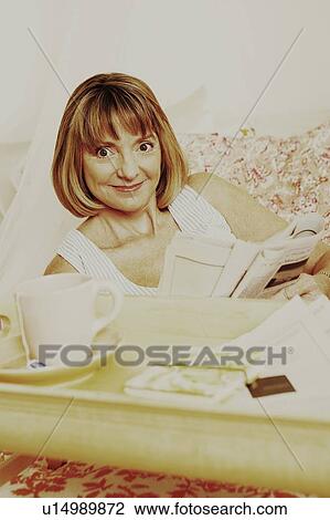 Stock Image - Portrait of a mature woman holding a newspaper and grinning. Fotosearch