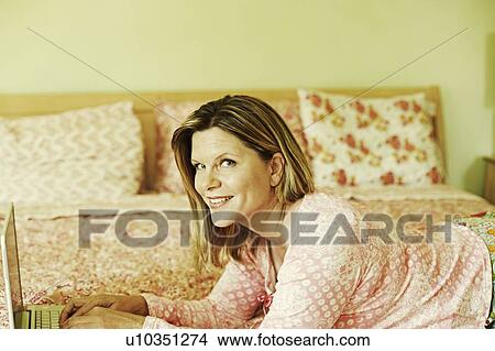 Portrait of a mature woman lying on the bed and using a laptop View Large Photo Image Picture - Portrait of a mature woman lying on the bed and using a laptop. Fotosearch