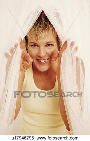 Stock Photography - Portrait of a mature woman peeking from a mosquito net. Fotosearch