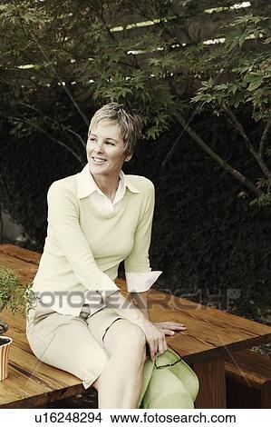 Portrait of a mature woman sitting on a table and smiling View Large Photo Image Picture - Portrait of a mature woman sitting on a table and smiling. Fotosearch