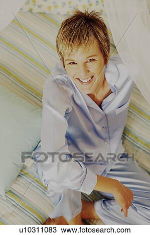 Portrait of a mature woman sitting on the bed and smiling View Large Photo Image Stock Image - Portrait of a mature woman sitting on the bed and smiling. Fotosearch