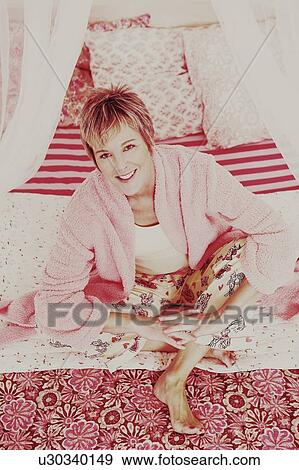 Portrait of a mature woman sitting on the bed and smiling View Large Photo Image Stock Photo - Portrait of a mature woman sitting on the bed and smiling. Fotosearch