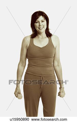 Stock Image - Portrait of a mature woman standing and holding dumbbells. Fotosearch