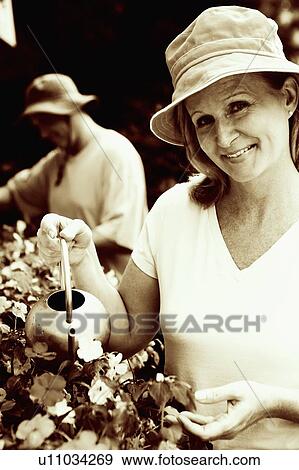 Portrait of a mature woman watering plants with a mature man in the background View Large Photo Image Stock Photo - Portrait of a mature woman watering plants with a mature man in the background. Fotosearch