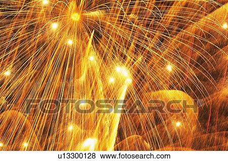 Stock Photo -  Bronze-colored Fireworks Exploding in the Night Sky, Long Exposure, Low Angle View. Fotosearch