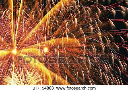 Stock Image -  Red and Orange-colored Fireworks Exploding in the Night Sky, Long Exposure, Low Angle View. Fotosearch
