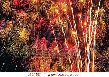 Stock Image -  Red and Orange-toned, Different-formed Fireworks, Exploding in the Night sky, Low Angle View, Long Exposure. Fotosearch