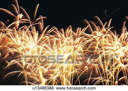 Stock Photo -  Several Small Yellow-colored Fireworks Exploding in the Night Sky, Long Exposure, Low Angle View . Fotosearch