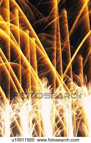 Stock Image -  Several White and Orange-colored Fireworks Exploding in the Night Sky, Long Exposure, Low Angle View . Fotosearch