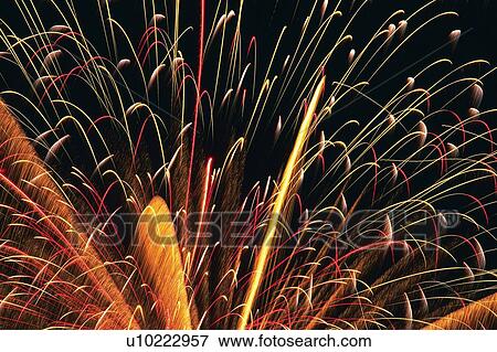 Stock Photo -  White and Orange-colored Fireworks Exploding in the Night Sky, Long Exposure, Low Angle View . Fotosearch