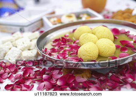 Stock Image - Close-up of a dish of Indian sweets with flower petals around it. Fotosearch