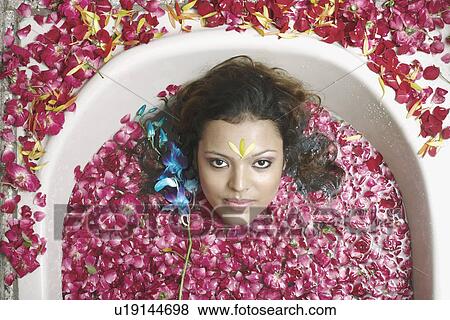 Stock Photo - High angle view of a young woman lying in a bathtub with flower petals floating. Fotosearch