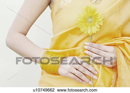 Stock Image - Mid section view of a young woman holding a flower. Fotosearch