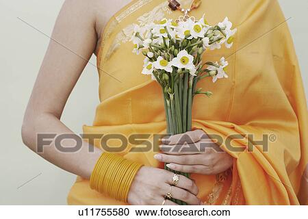 Stock Image - Mid section view of a young woman holding flowers. Fotosearch