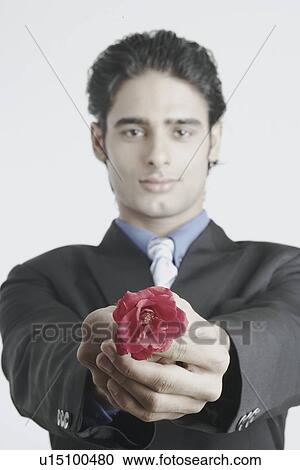 Stock Image - Portrait of a young man holding out a rose. Fotosearch