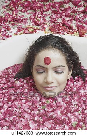 Stock Image - Portrait of a young woman lying in a bathtub covered with flower petals. Fotosearch