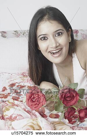 Stock Photography - Portrait of a young woman lying on the bed holding roses. Fotosearch