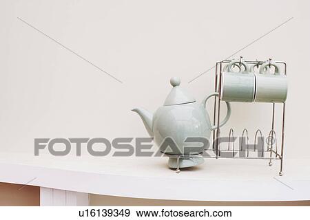 Stock Photo - Close-up of a tea cup and a tea kettle on a rack. Fotosearch