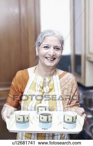 Stock Image - Portrait of a mature woman holding a tray with cups. Fotosearch