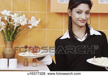 Stock Photo - Portrait of a young woman holding plates of noodles and salad. Fotosearch