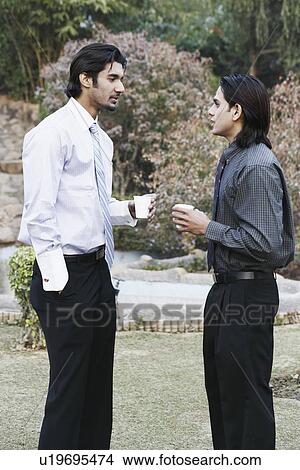 Picture - Side profile of two businessmen talking in the garden. Fotosearch