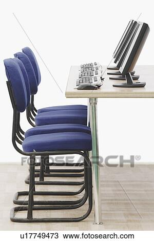 Stock Image - Computer on a table in front of chairs. Fotosearch