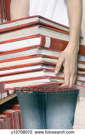 Stock Image - Mid section view of a woman carrying a stack of books in a library. Fotosearch