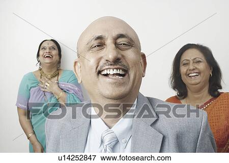 Stock Photo - Portrait of a mature man laughing with two mature women standing behind him. Fotosearch