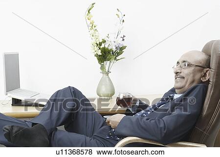 Stock Photo - Side profile of a businessman reclining on a chair and holding a cup of black tea. Fotosearch