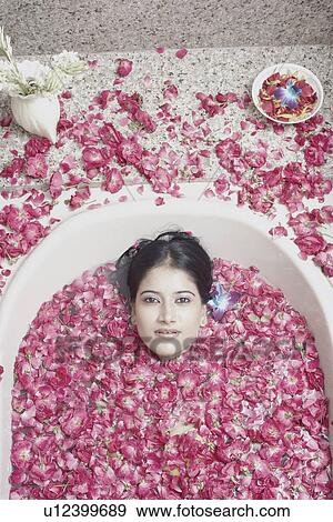 Stock Photo - High angle view of a young woman lying in a bathtub covered with flower petals. Fotosearch