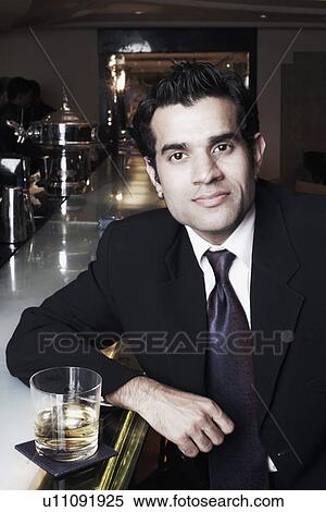 Stock Photography - Portrait of a businessman sitting at a bar counter with a glass of whiskey. Fotosearch