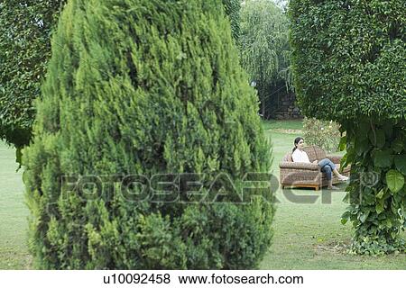 Stock Photo - Side profile of a young woman sitting on a couch outdoors. Fotosearch