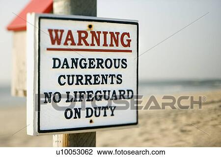 Stock Image - Warning sign on post at the beach with ocean in background.. Fotosearch