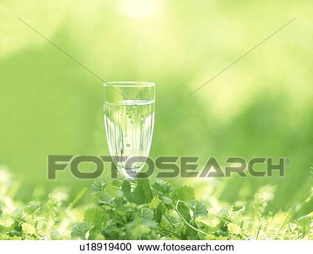 Stock Image - Glass of water against green background. Fotosearch