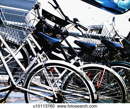 Stock Image - Bicycles parked along roadside near a white car. Fotosearch