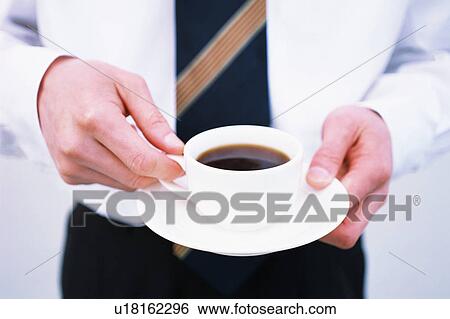Stock Photograph - Close up of a cup of coffee held by a business man. Fotosearch