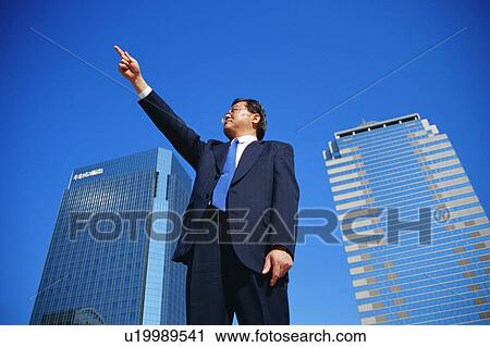 Stock Image - Low angle view of a mature man pointing towards sky. Fotosearch